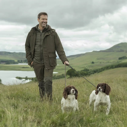 Man walking two spaniel dogs in a grassy field wearing Fife Kincraig Waterproof Field Jacket