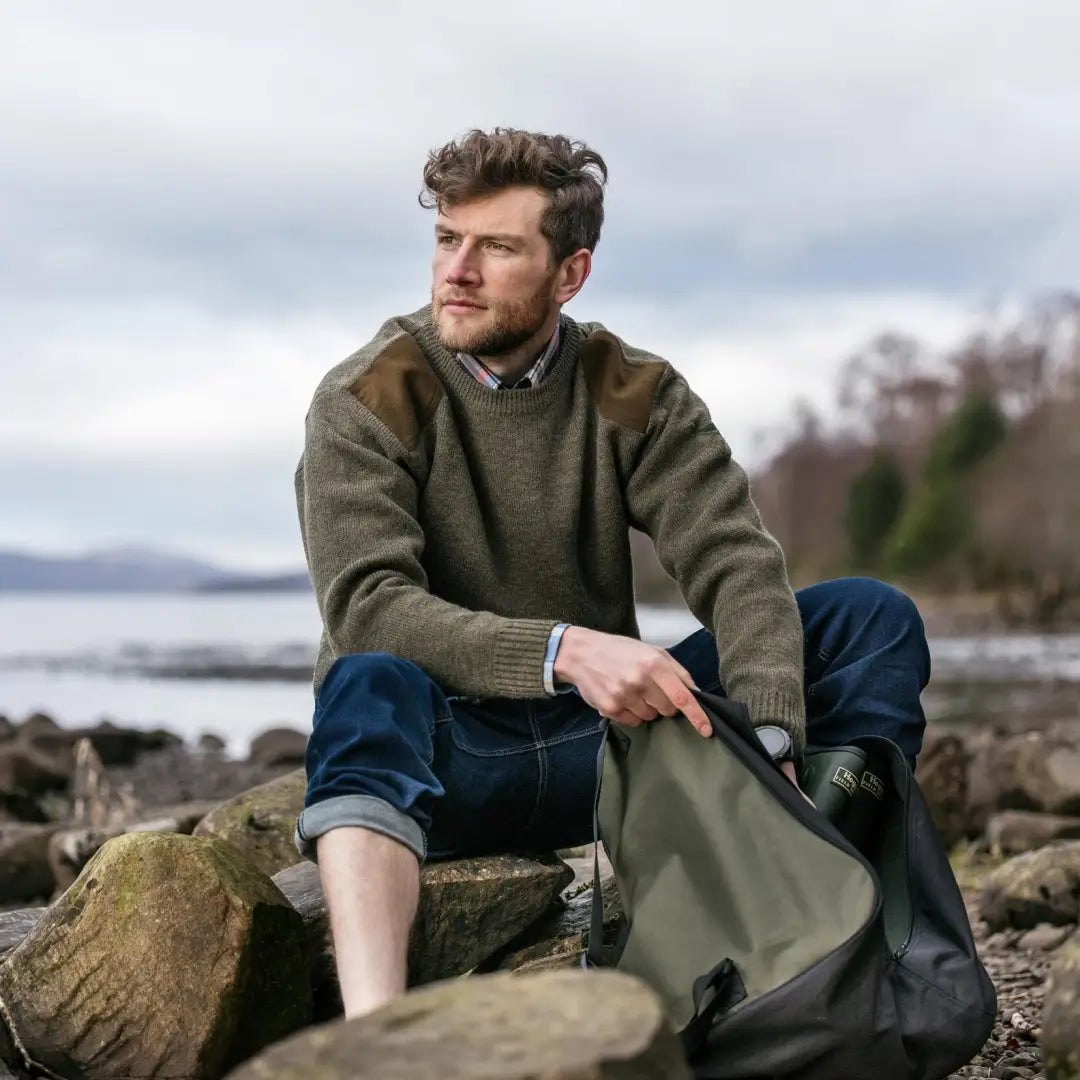 Man in a green sweater and jeans by the sea with Fife Melrose Hunting Pullover