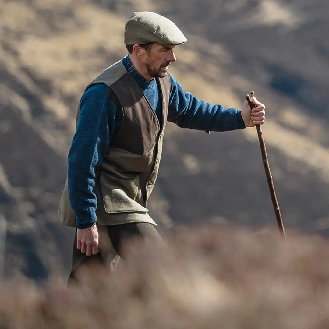 Man in flat cap and vest hiking in country clothing with a walking stick outdoors