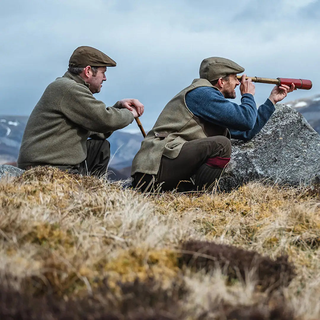 Two men in countryside attire on a hill, one using a telescope in Melrose Hunting Pullover