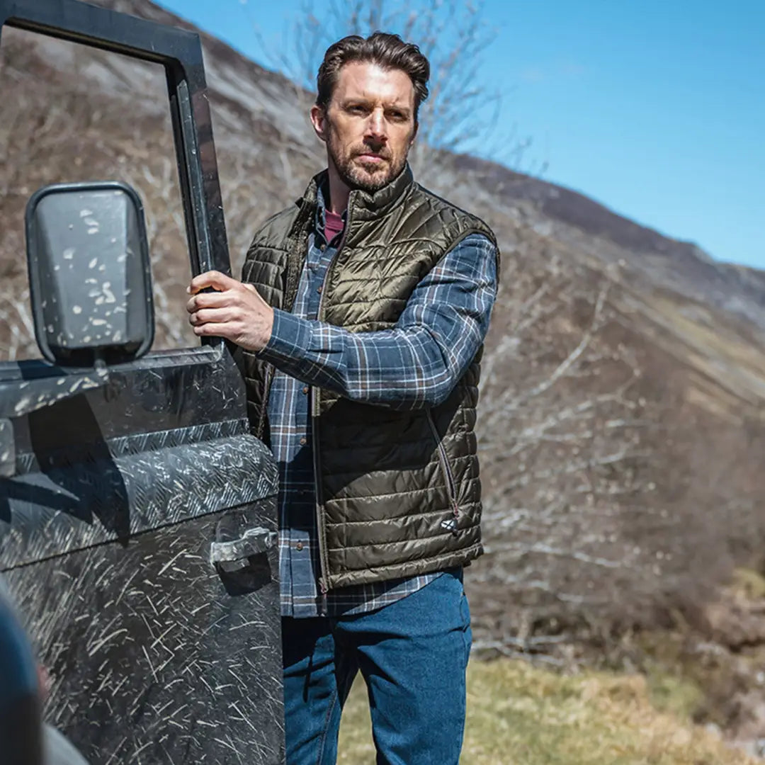 Man in a quilted vest and plaid shirt by a vehicle door showcasing Pitlessie Shirt features