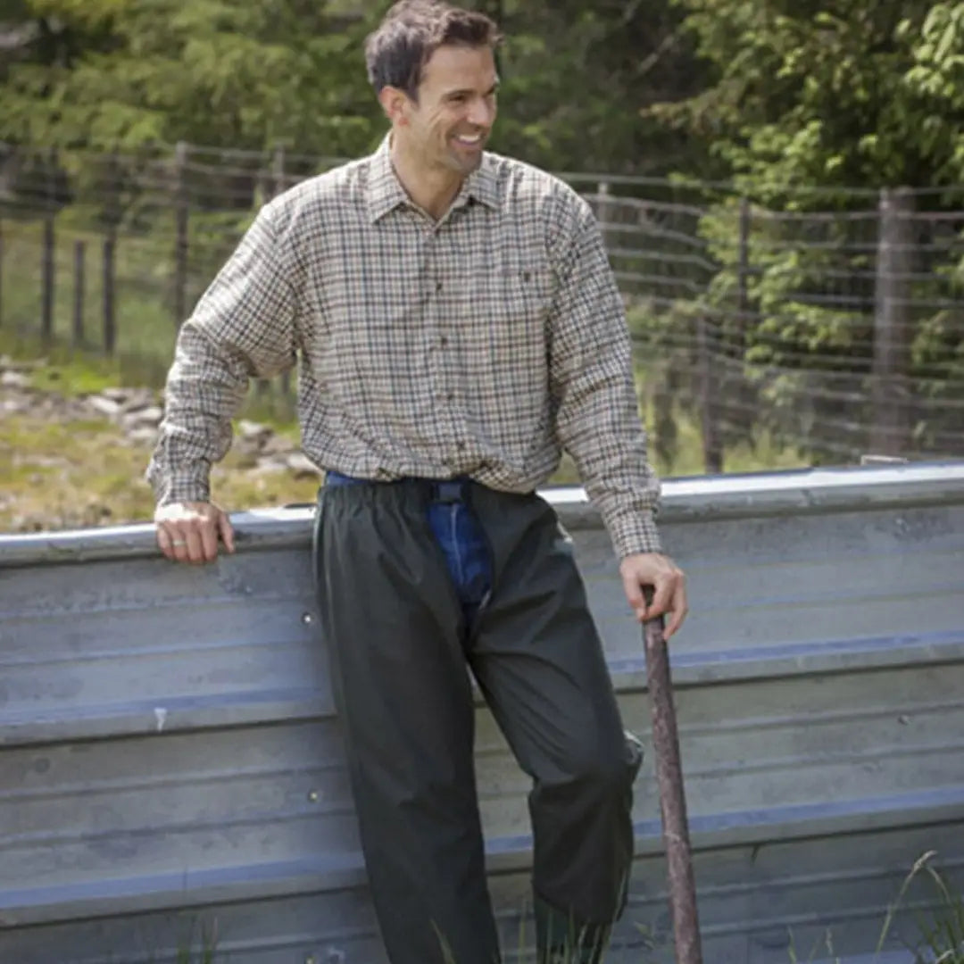 Man in plaid shirt and dark pants wearing Fife Waxed Treggings, leaning on a fence