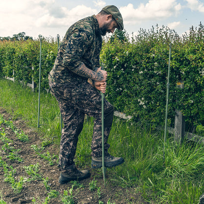 Camouflaged man planting stakes in Jack Pyke Armour Long Sleeved Top for outdoor adventures