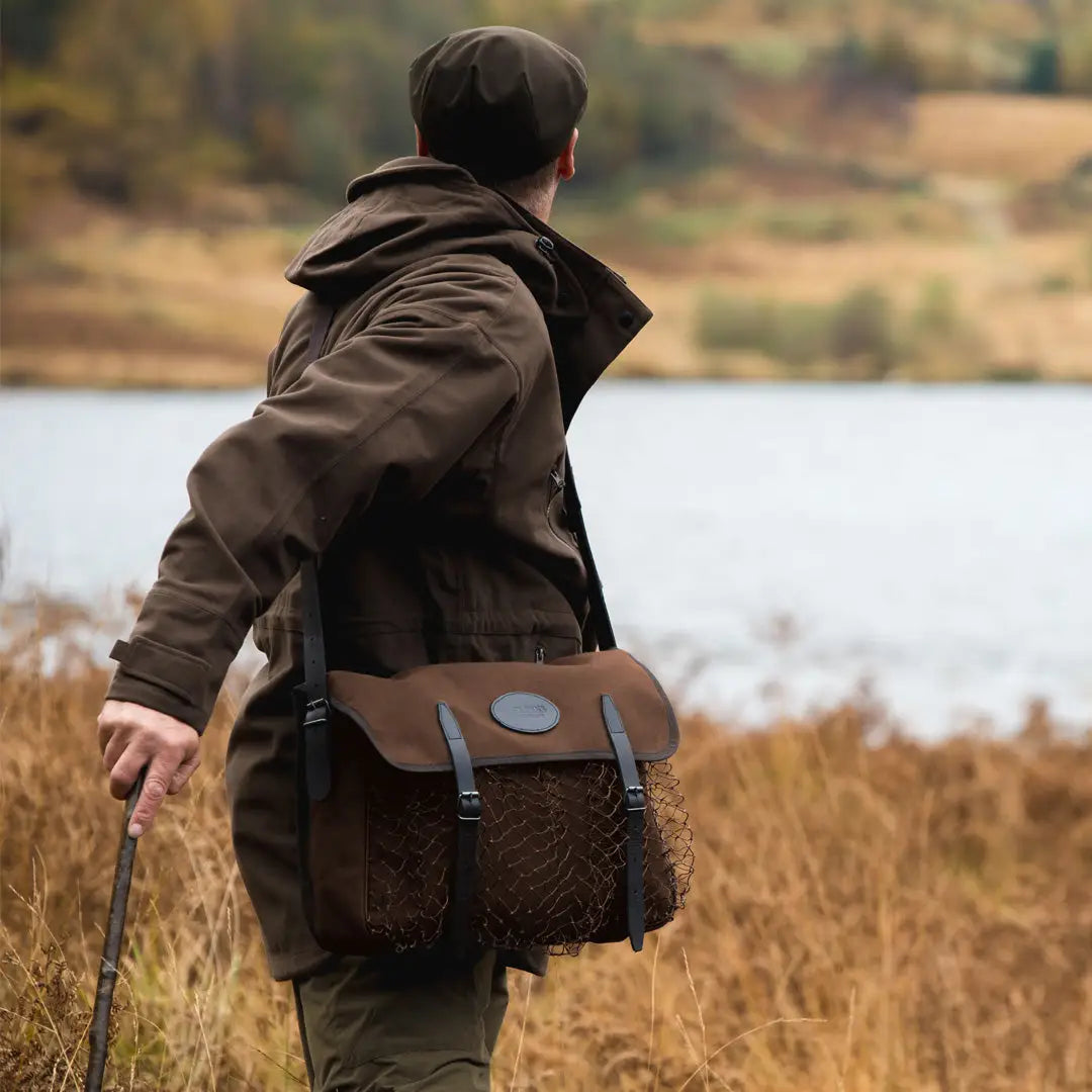 Person in a brown coat by water, showcasing the stylish Jack Pyke Canvas Game Bag