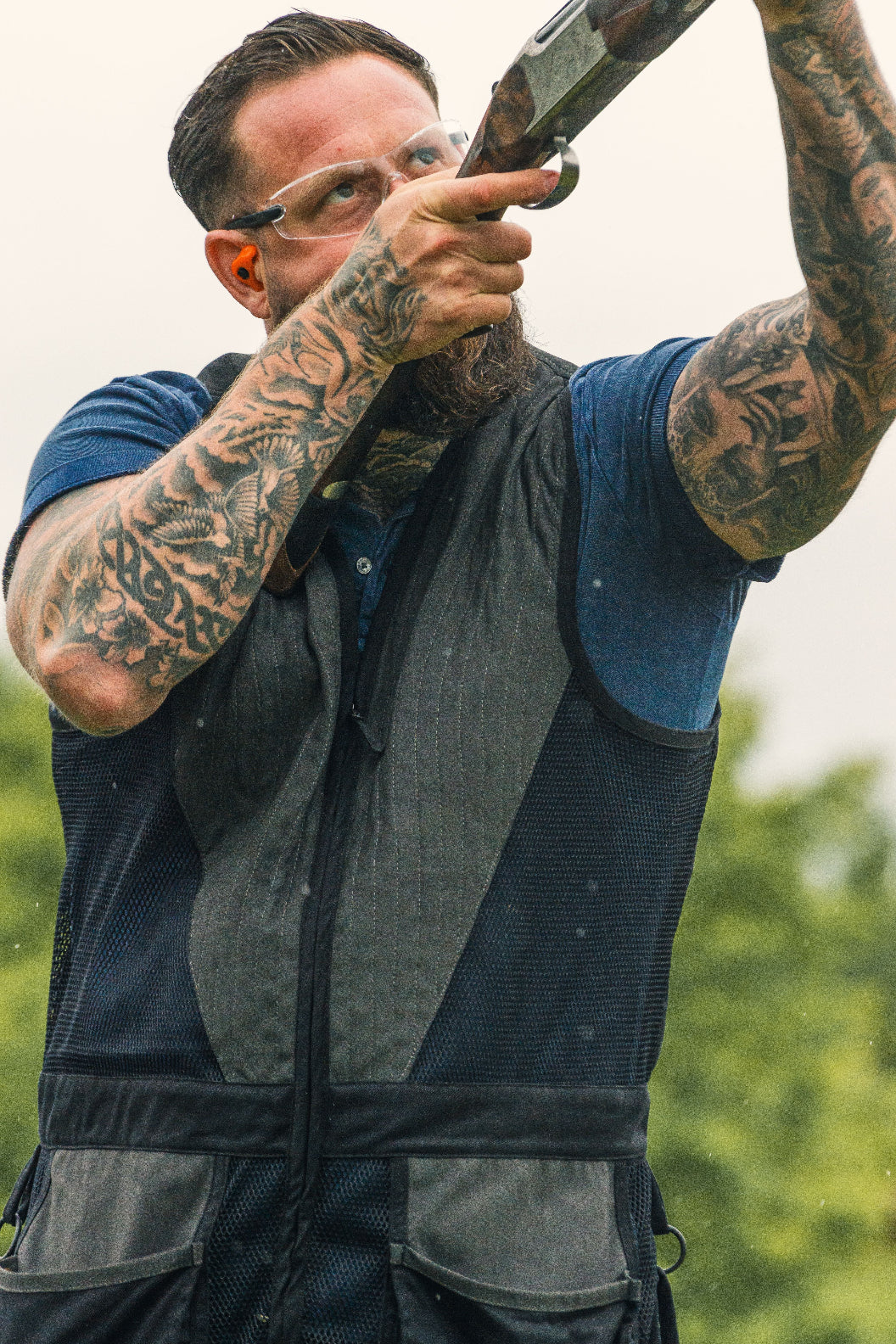 Tattooed man aiming shotgun while wearing Jack Pyke Sporting Skeet Vest