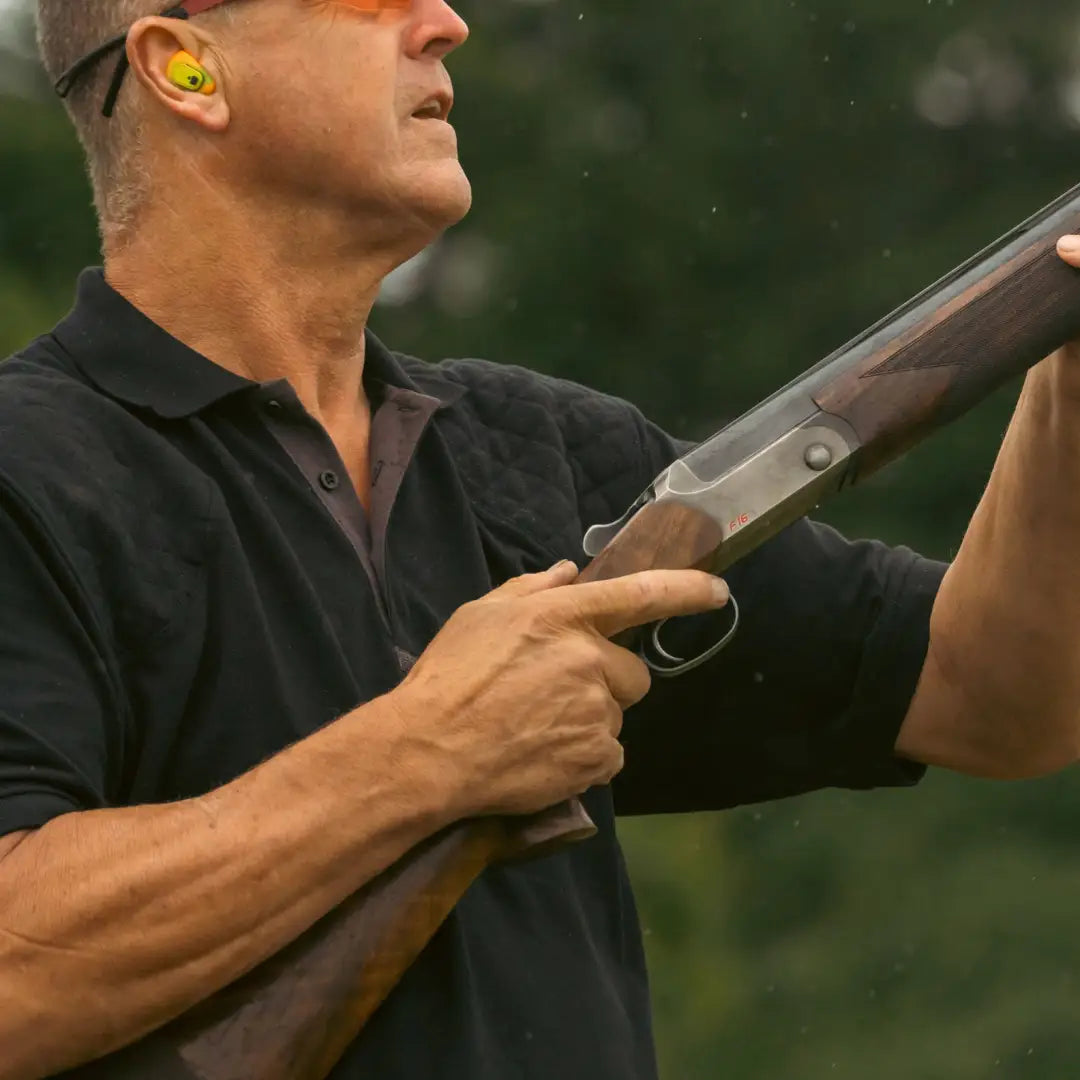 Person in black Jack Pyke polo shirt holding a shotgun with yellow ear protection