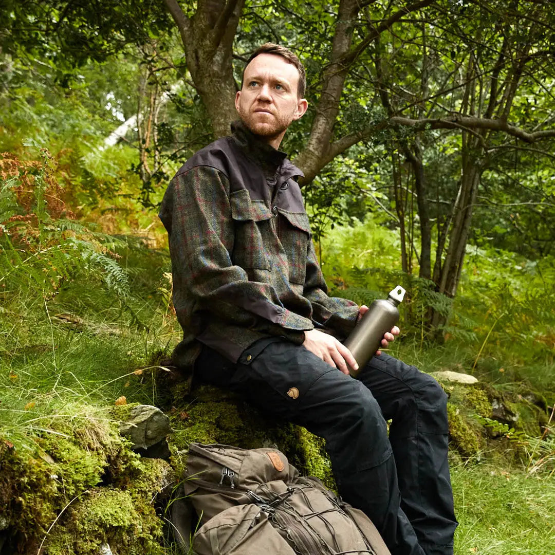 Man in Keela Harris Tweed Smock sits on a rock, enjoying nature with a water bottle