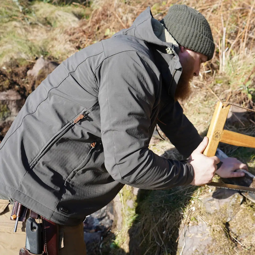 Person in a Keela Hydron Softshell Jacket inspecting a wooden object outdoors