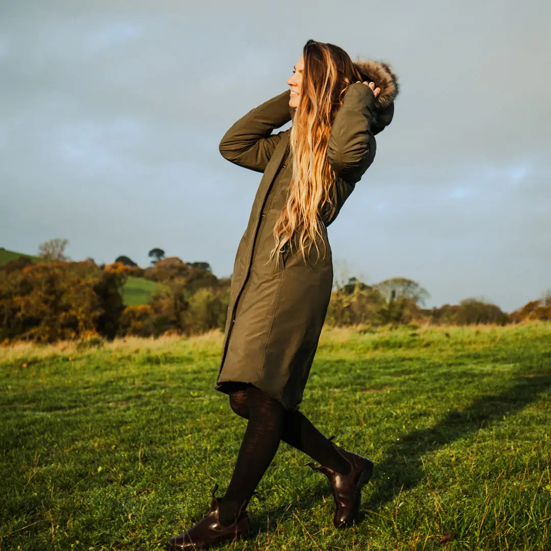 Long-haired person in olive green Crofter Parka in a grassy field, perfect for country clothing