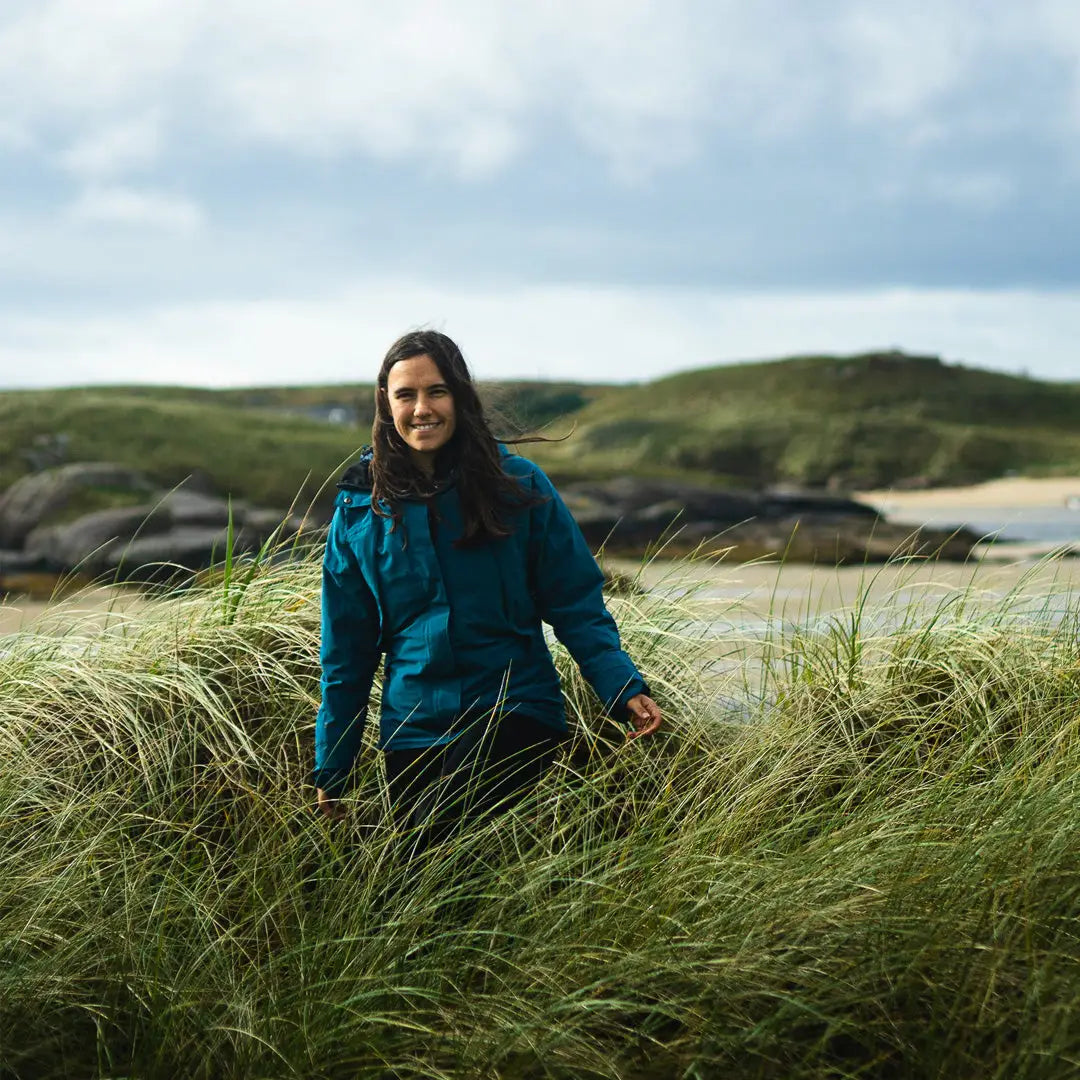 Woman in a teal Keela Womens Prosport Jacket standing in tall grass, ready for adventure