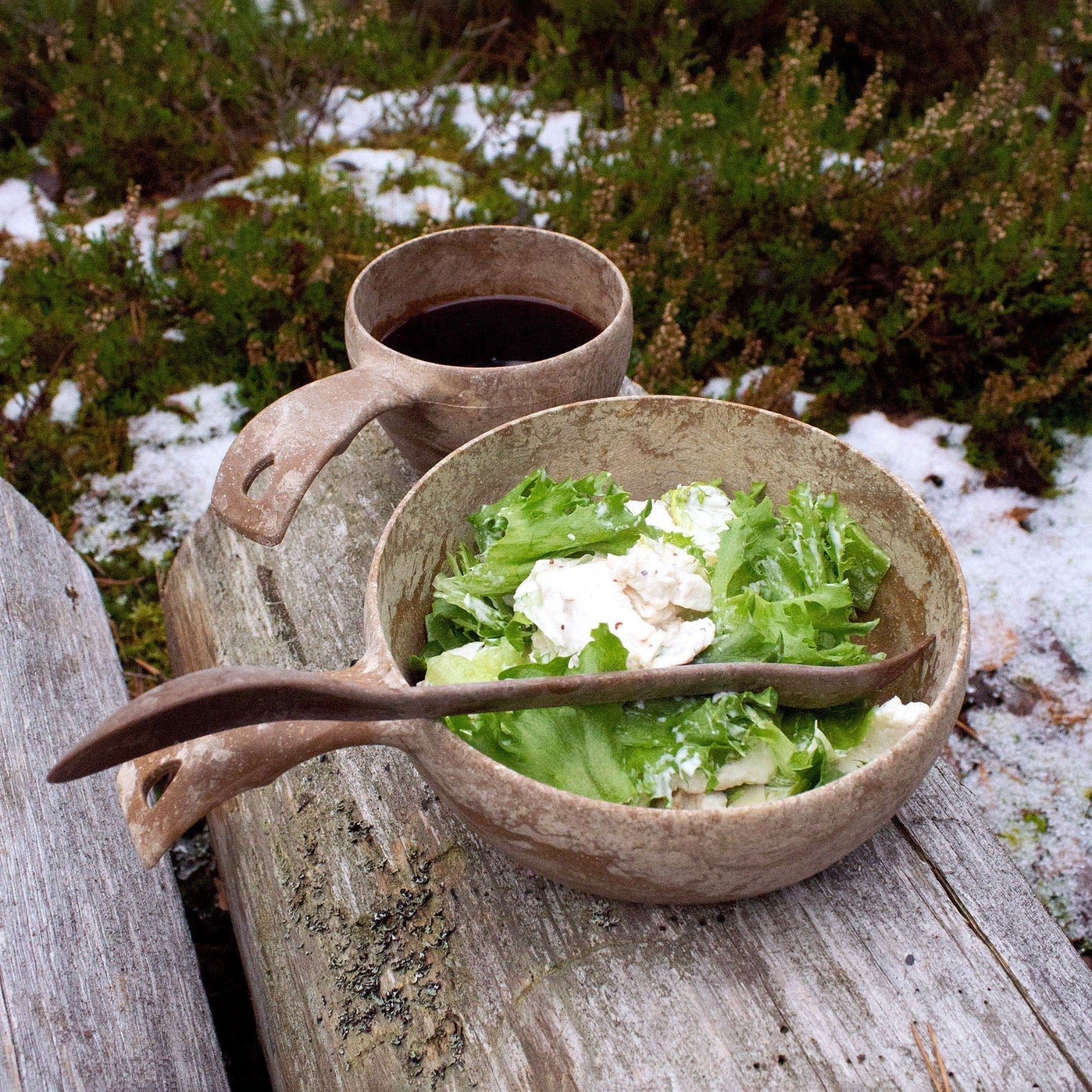 Hand-carved wooden bowl with salad and dark drink for your outdoors dining vibe