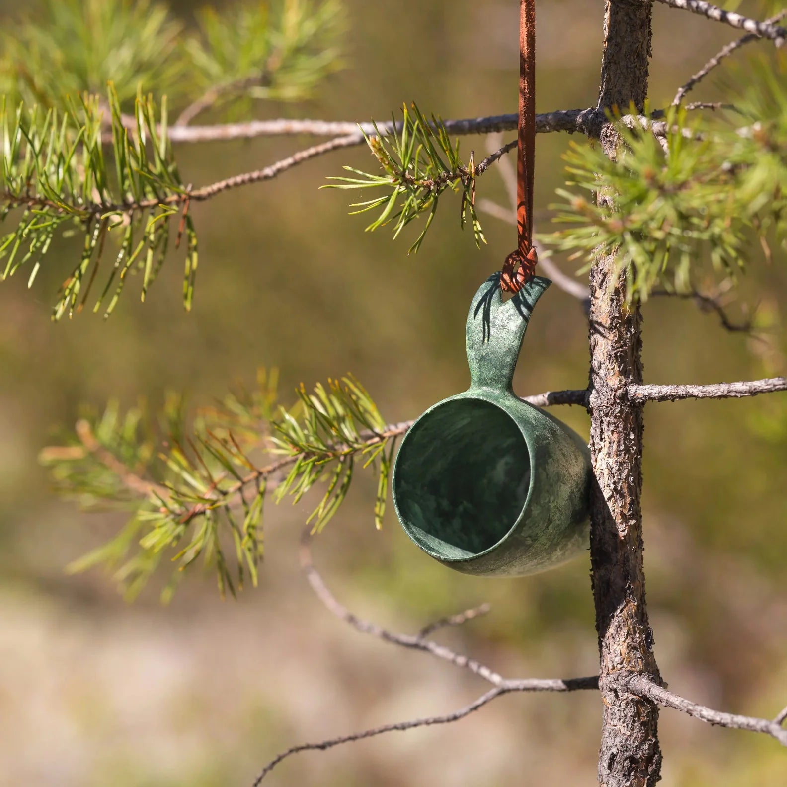 Green wooden Kupilka Shot Cup hanging from a tree, perfect for country clothing and hunting