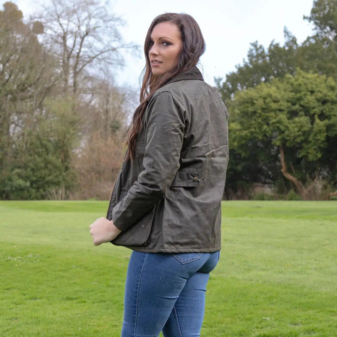 Woman in a green Antique Wax Jacket and blue jeans standing in grass