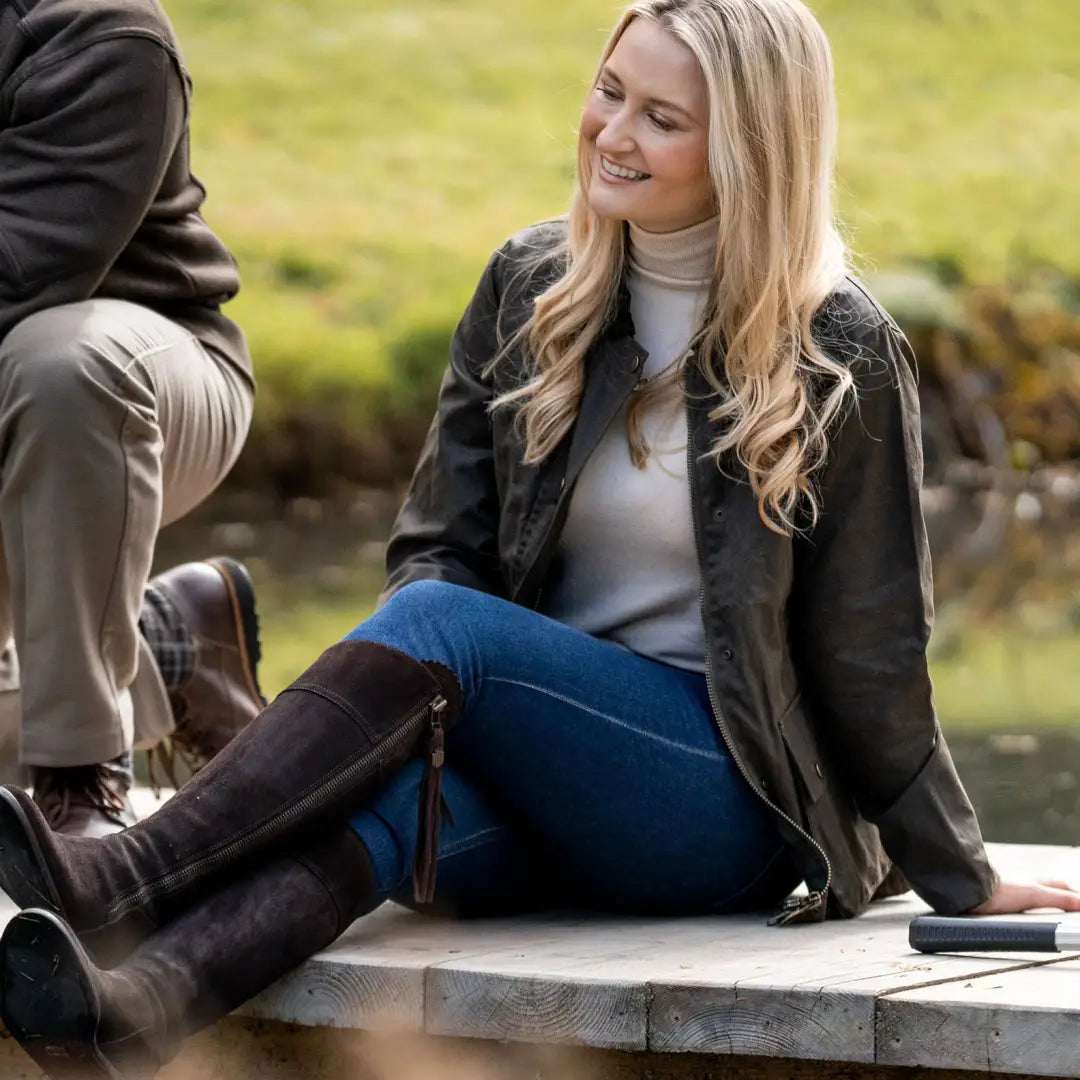 Smiling blonde woman outdoors in a dark Antique Wax Jacket and stylish boots