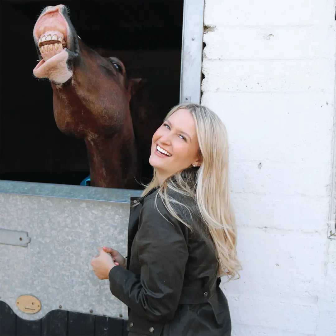 Smiling horse behind woman in Ladies Antique Wax Jacket with long blonde hair