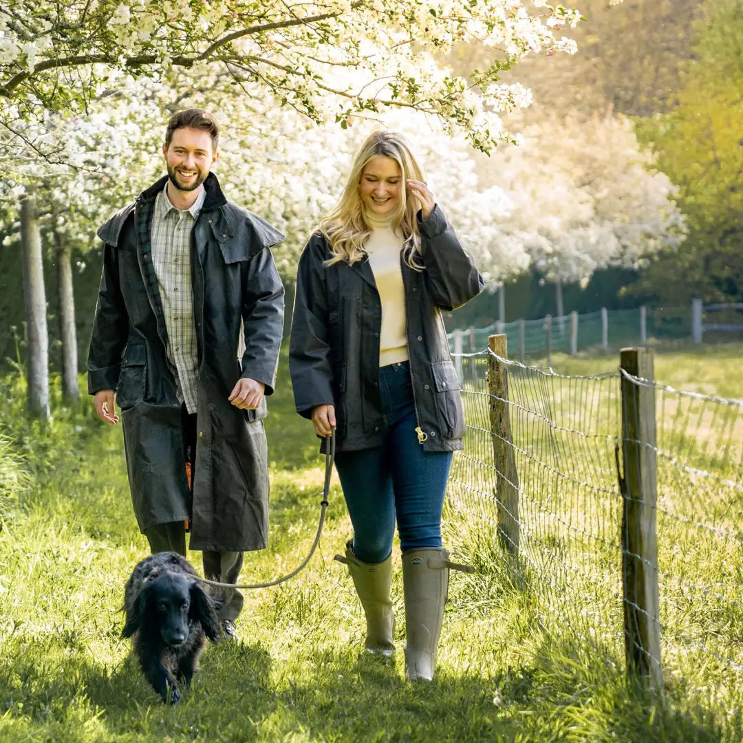 Couple in a padded wax jacket walking a dog under cherry blossoms in spring