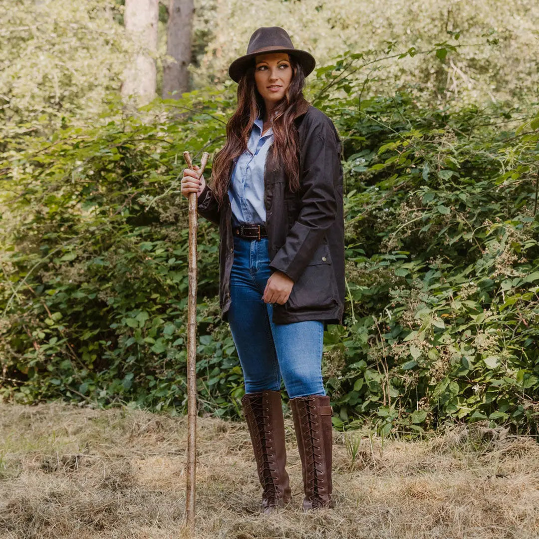 Woman in country-style attire with a walking stick wearing a traditional wax jacket