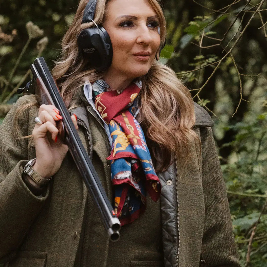 Woman in a ladies tweed jacket with shotgun and headphones in outdoor setting