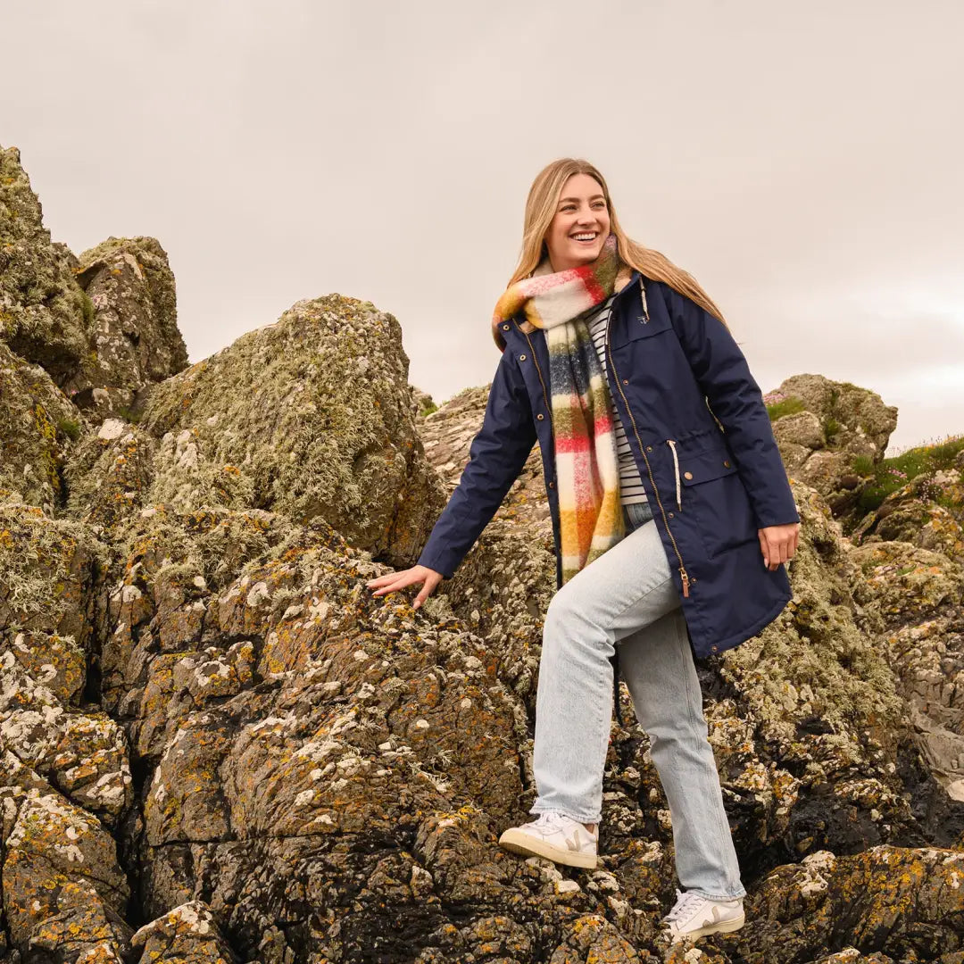 Woman in a navy blue Lighthouse Isobel Coat with a colorful scarf on rocky terrain