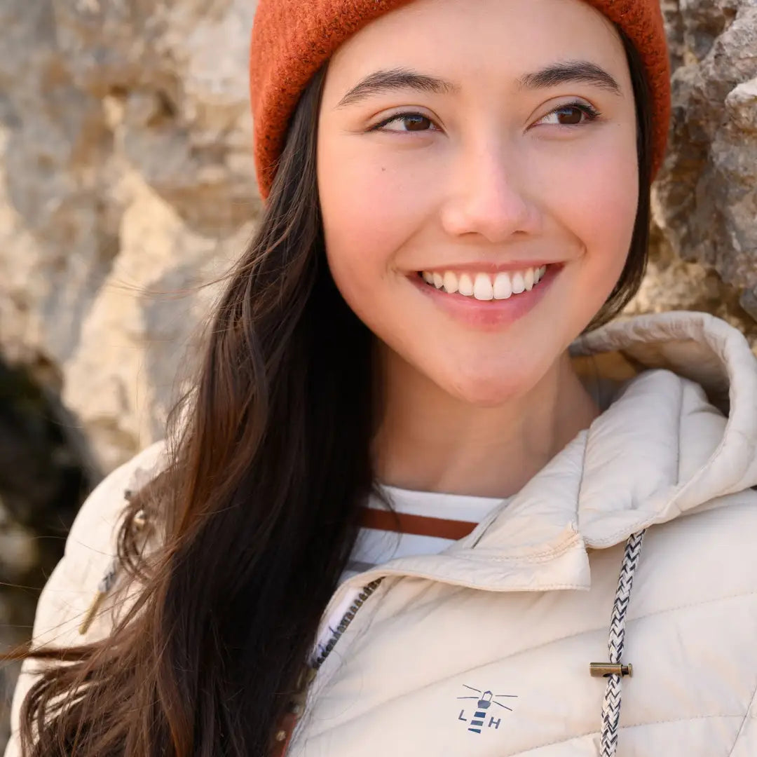 Smiling woman in an orange beanie and white mid-length coat outdoors showcasing coat offers