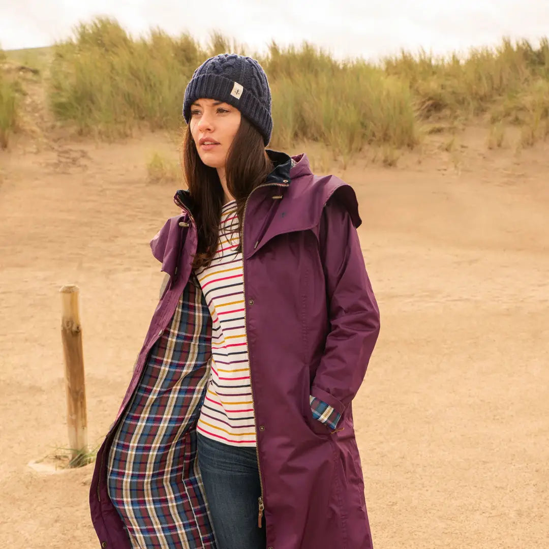 Woman in a purple coat and navy hat by the beach, showcasing Lighthouse Outback style