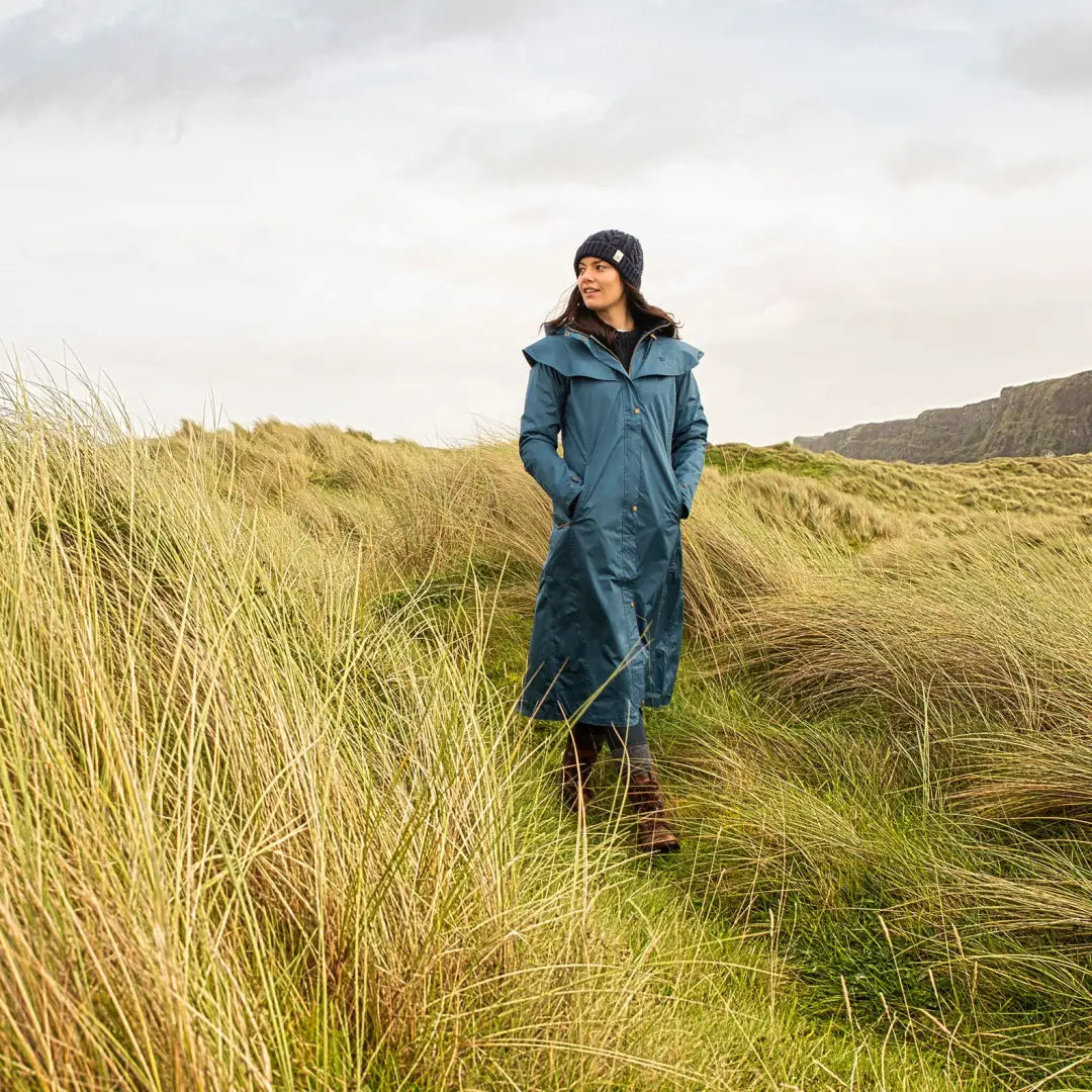 Woman in a long blue Lighthouse Outback waterproof coat standing in tall grass