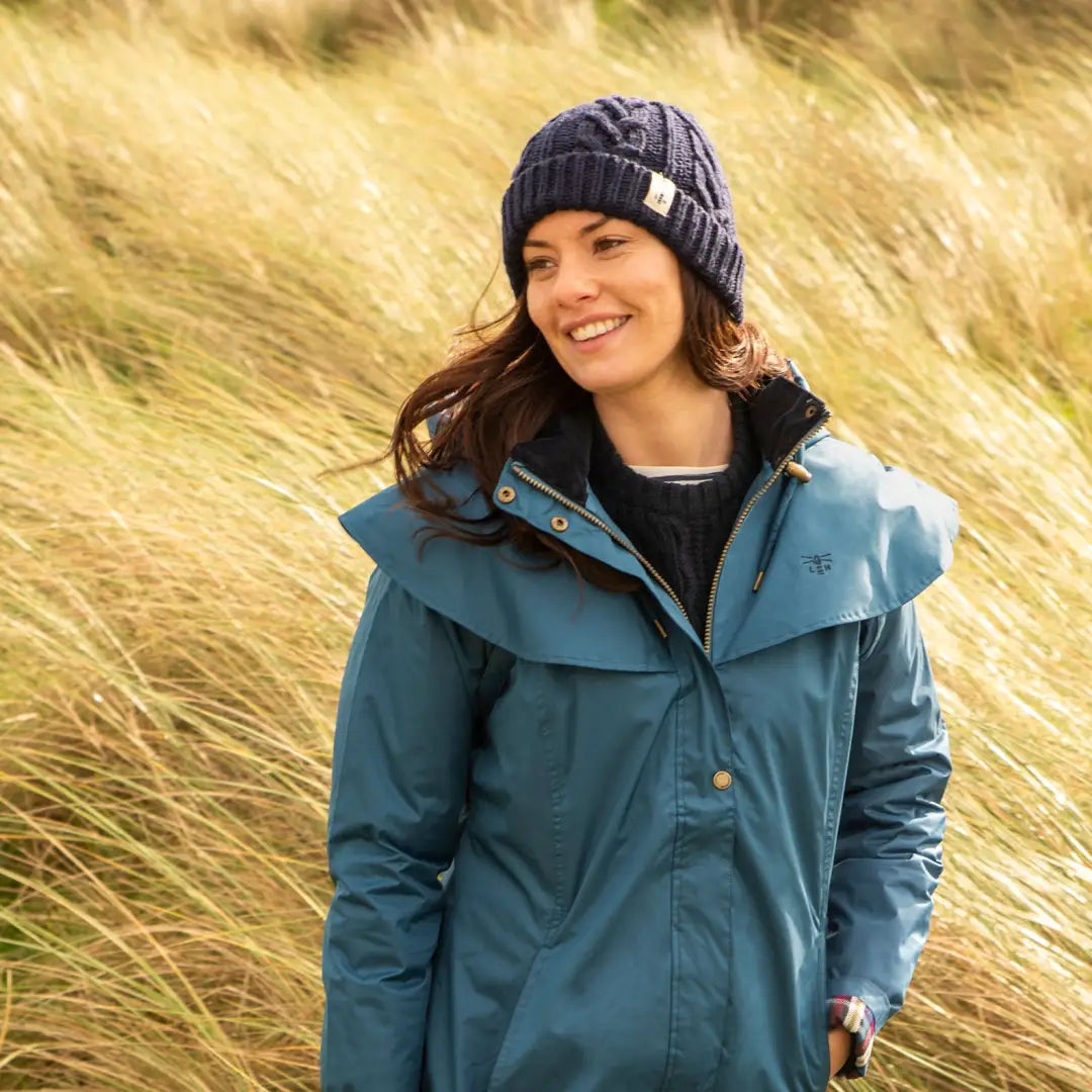 Woman in a teal Lighthouse Outrider waterproof raincoat in a grassy field