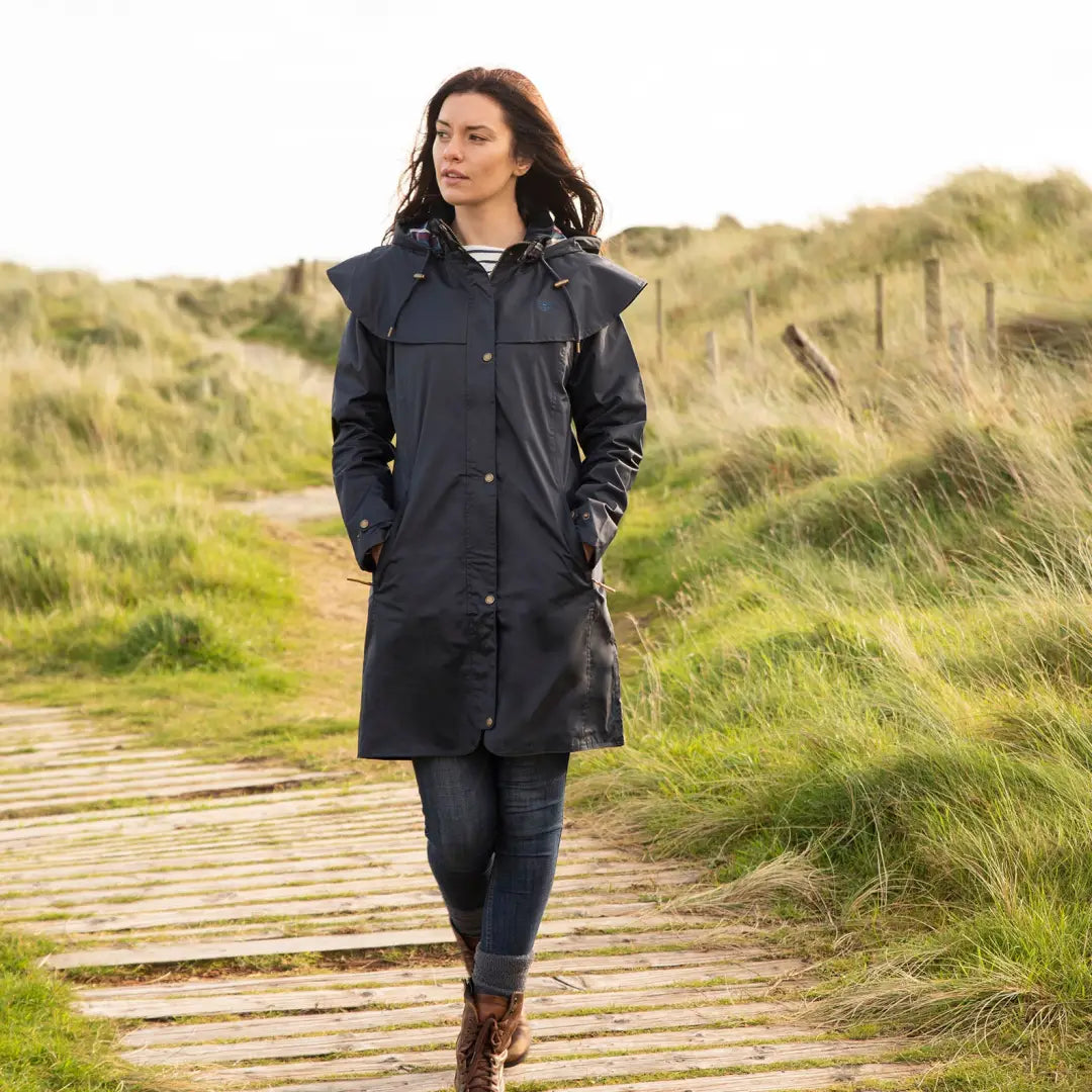 Woman in a long navy blue raincoat walking on a path, Lighthouse Outrider ladies waterproof