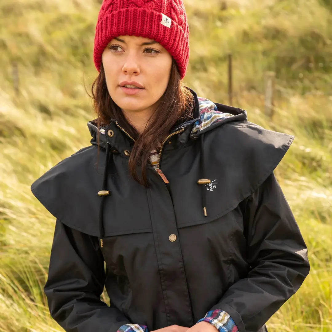 Woman in a red knit hat and black jacket wearing a Lighthouse Outrider ladies waterproof raincoat