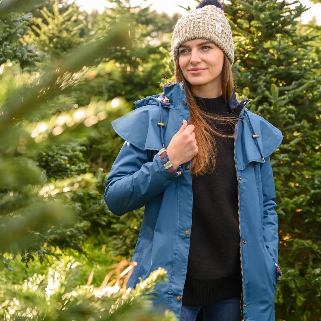 Woman in a blue coat and knit hat with evergreen trees in Lighthouse Outrider waterproof raincoat