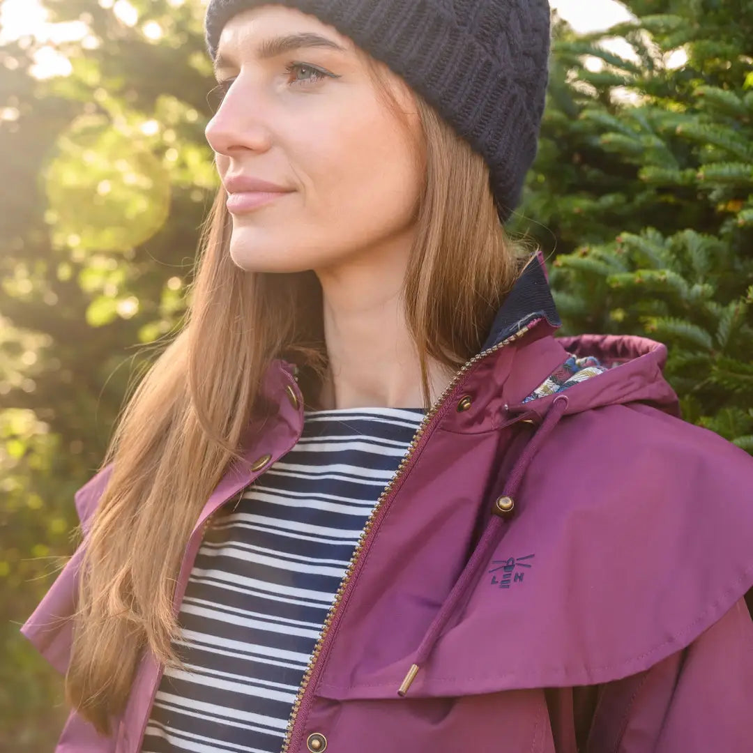 Woman in a black knit hat and purple jacket wearing a Lighthouse Outrider ladies waterproof raincoat