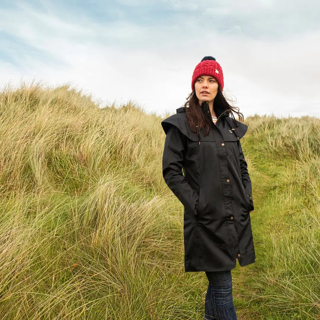 Woman in a black coat and red knit hat wearing a Lighthouse Outrider ladies waterproof raincoat