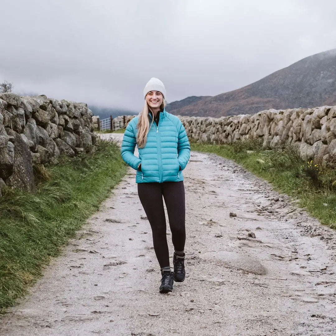 Woman in turquoise puffer jacket and knit hat enjoying country clothing outdoors