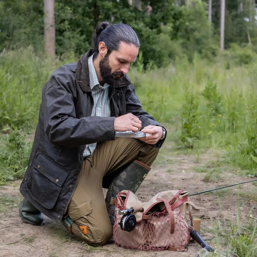 Man with beard and ponytail in Mens Classic Antique Wax Jacket using smartphone on dirt path