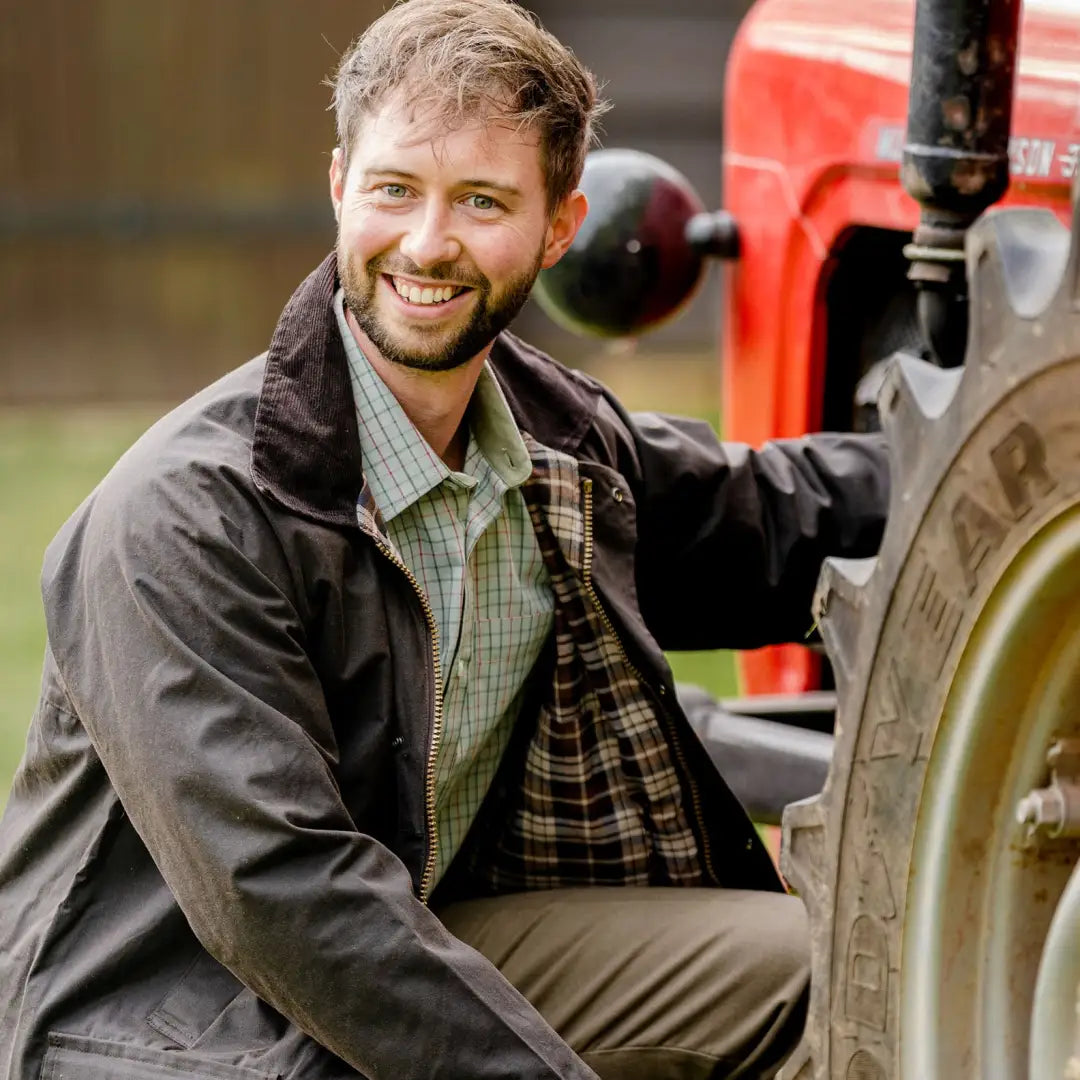 Smiling man in a traditional wax jacket next to a red tractor in the forest