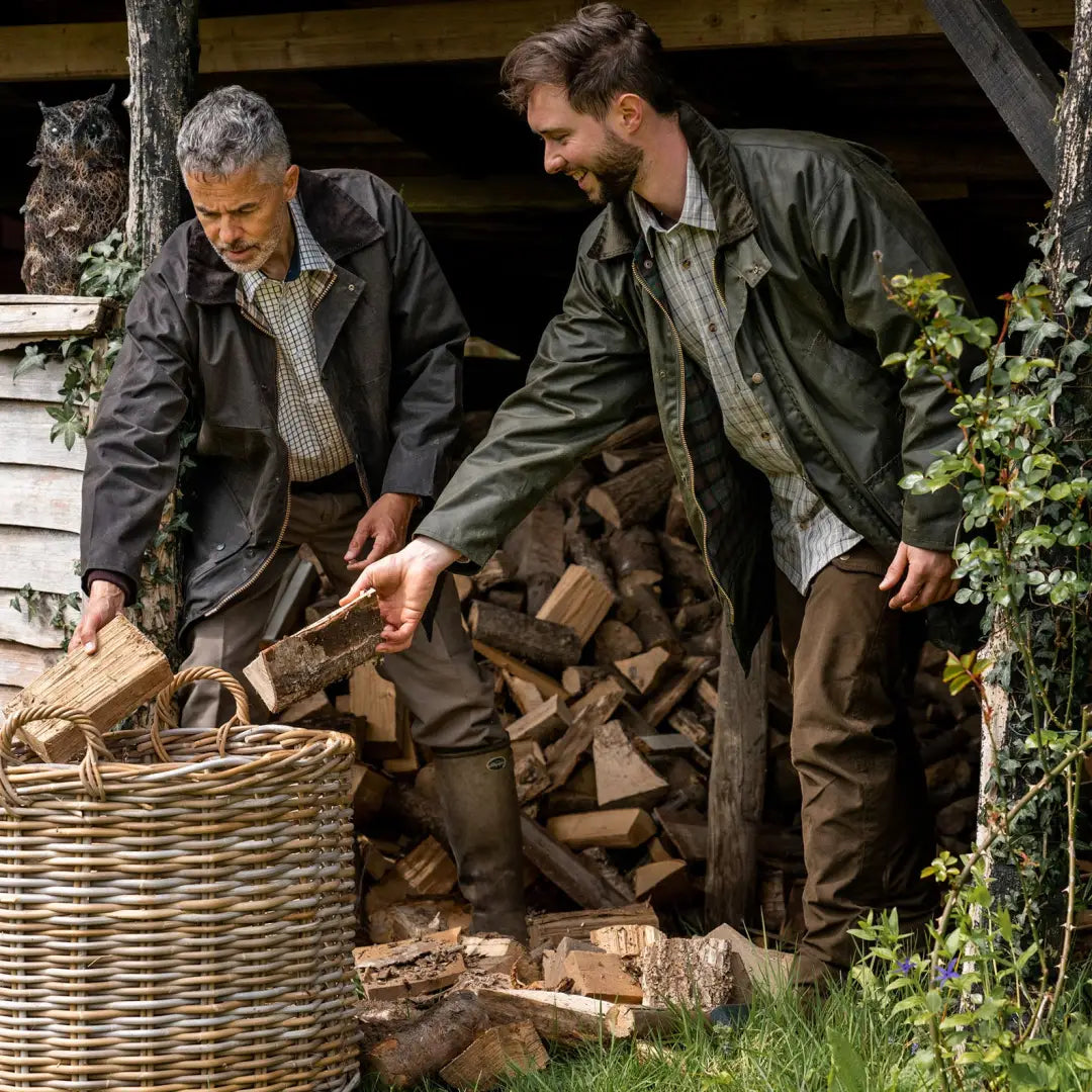 Two men wearing a traditional wax jacket gather firewood in a wicker basket