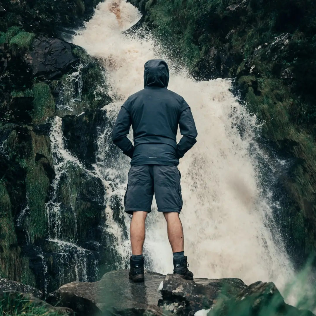 Person in Musto Land Rover Lite Rain Jacket on rock by a stunning waterfall