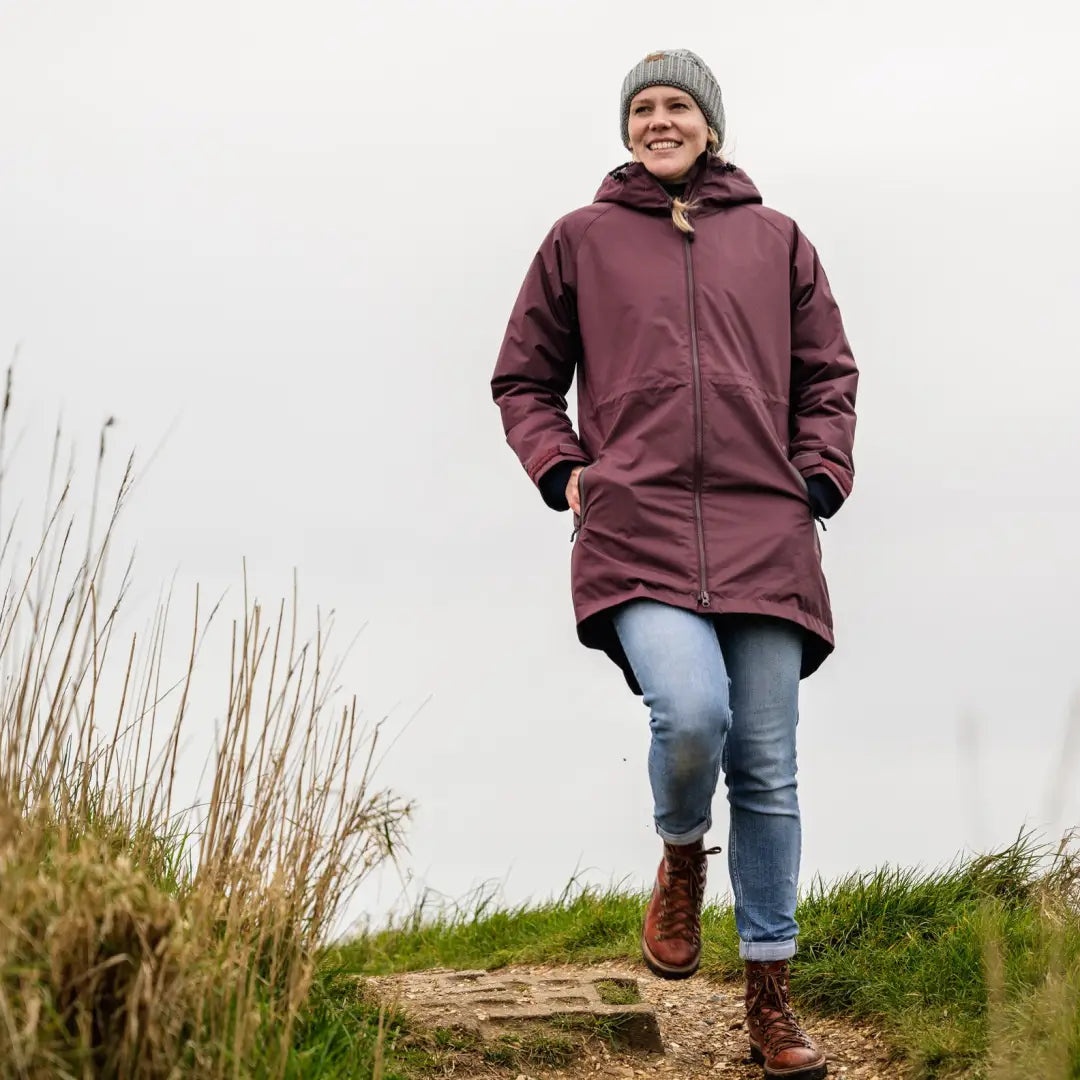 Woman in a burgundy Musto Corsica Long Primaloft jacket and gray hat on a path