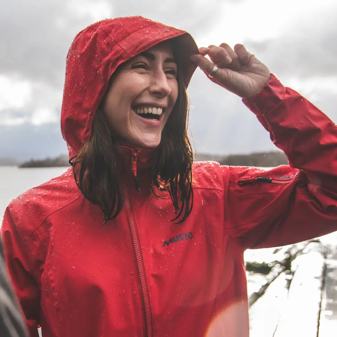 Smiling person in a bright red Musto Womens Sardinia Long Rain Jacket with hood