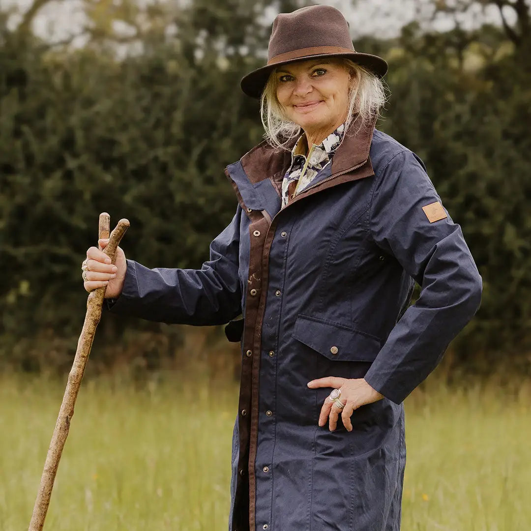 Smiling older woman in outdoor gear with a walking stick wearing Forest Alice Waterproof Coat