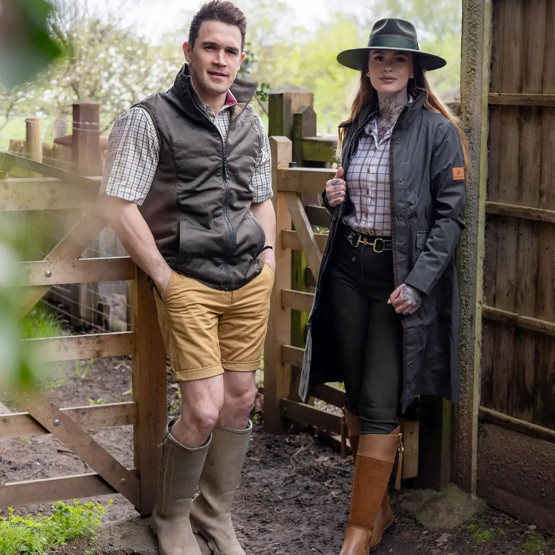 Two people in country-style clothes by a wooden fence wearing Forest Alice Waterproof coat