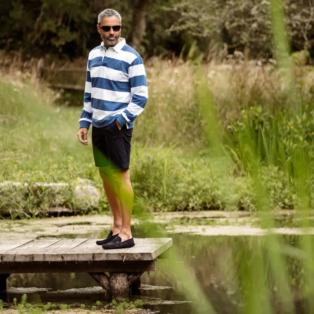 Man in a striped rugby shirt shows off New Forest Chino Shorts by a tranquil pond