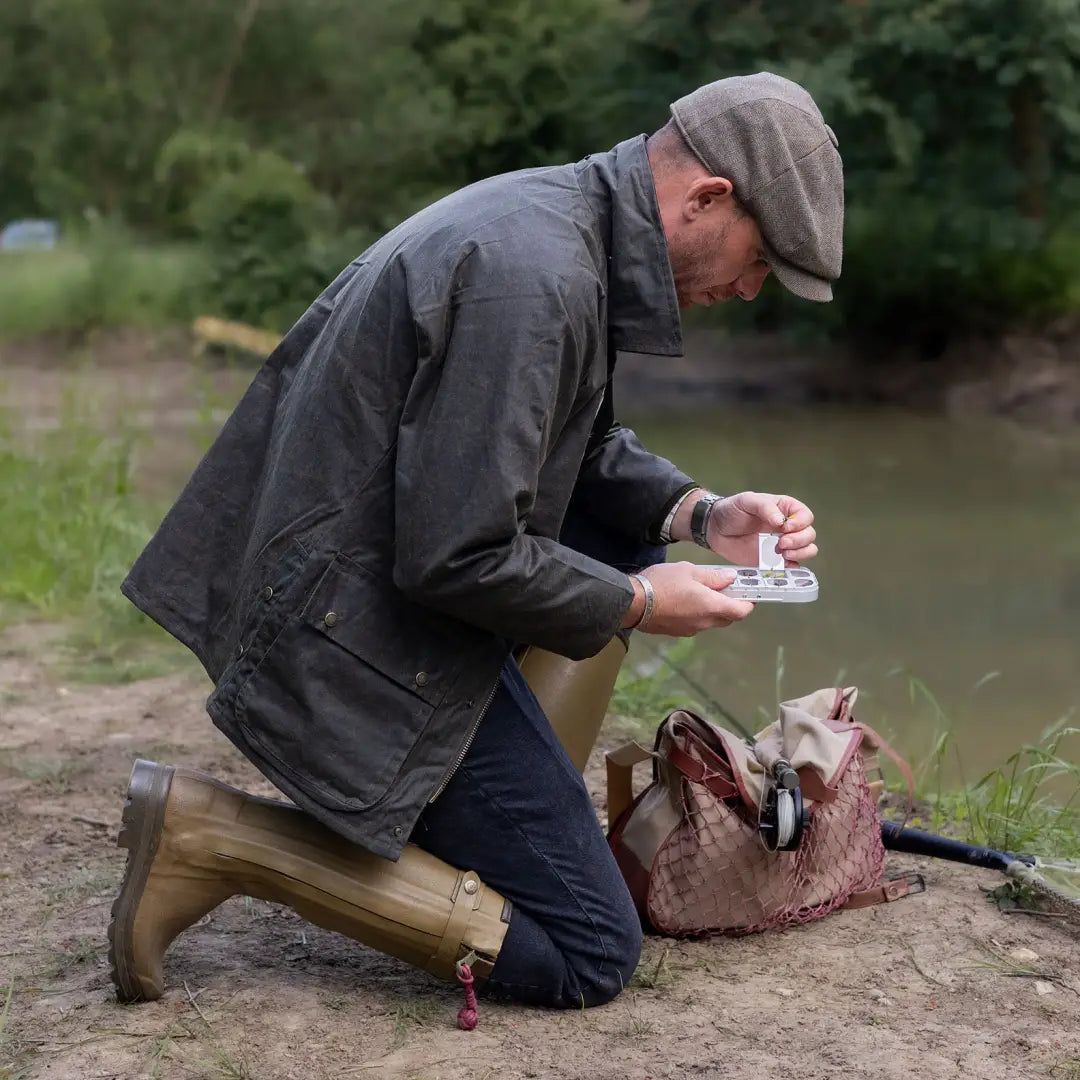 Person in a Mens Classic Antique Wax Jacket examining something by the river bank