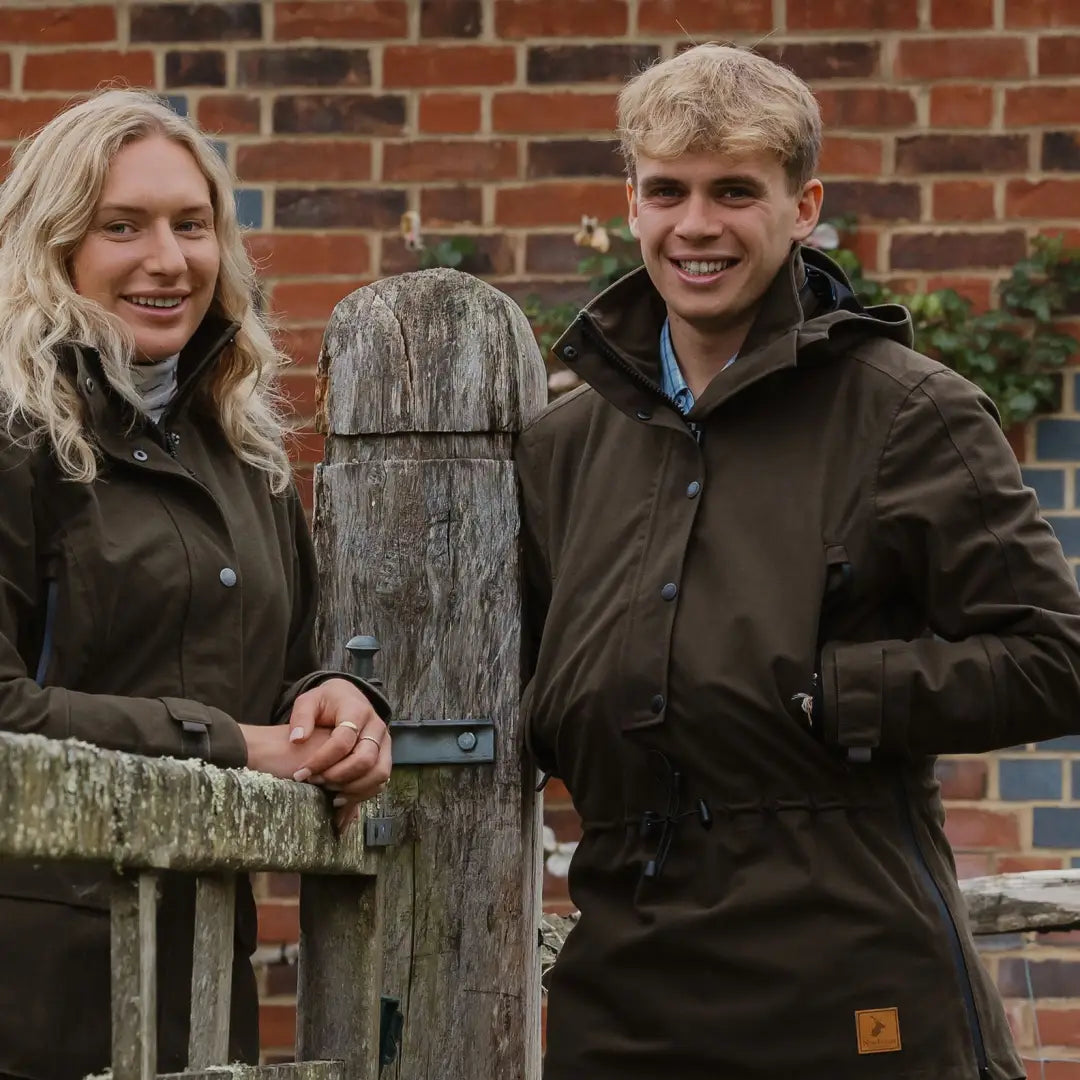 Two smiling young people by a wooden fence wearing the Forest Country Sport Smock