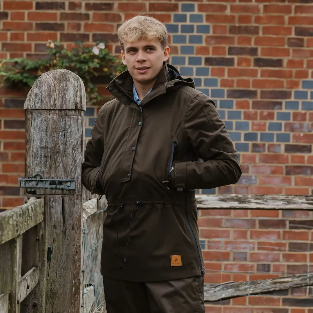 Young man in a dark brown country sport smock by a wooden fence in the forest