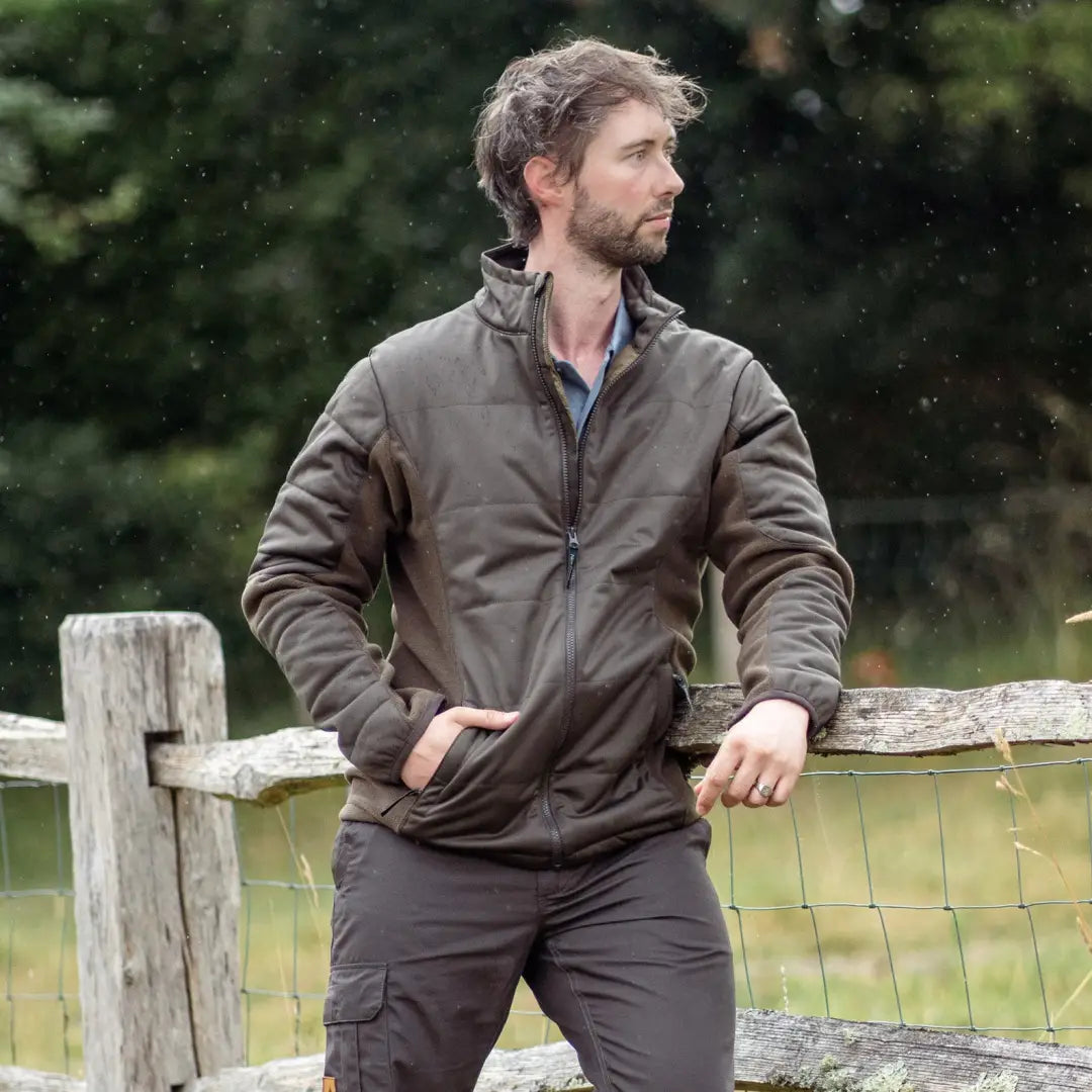 Man with a beard in a brown New Forest Falcon Padded Jacket by a wooden fence