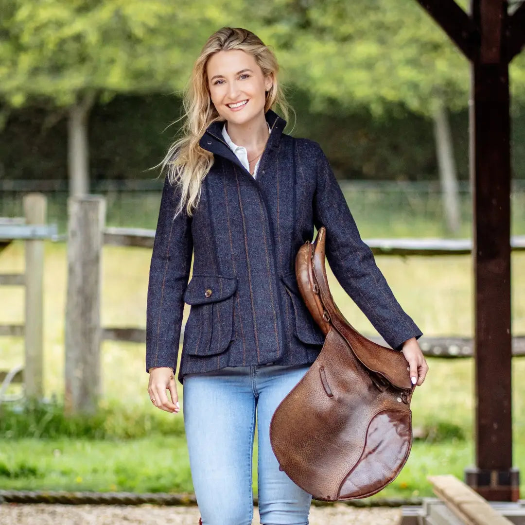 Woman in a navy blue jacket holding a brown leather saddle, showcasing the premium Forest Florence Tweed