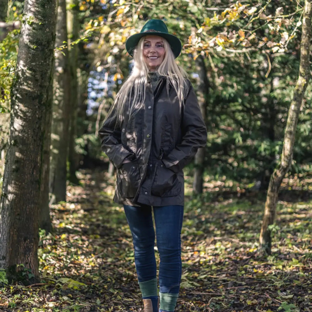 Woman in a hat and jacket on a forest path wearing the Forest Freya Ladies Wax Jacket