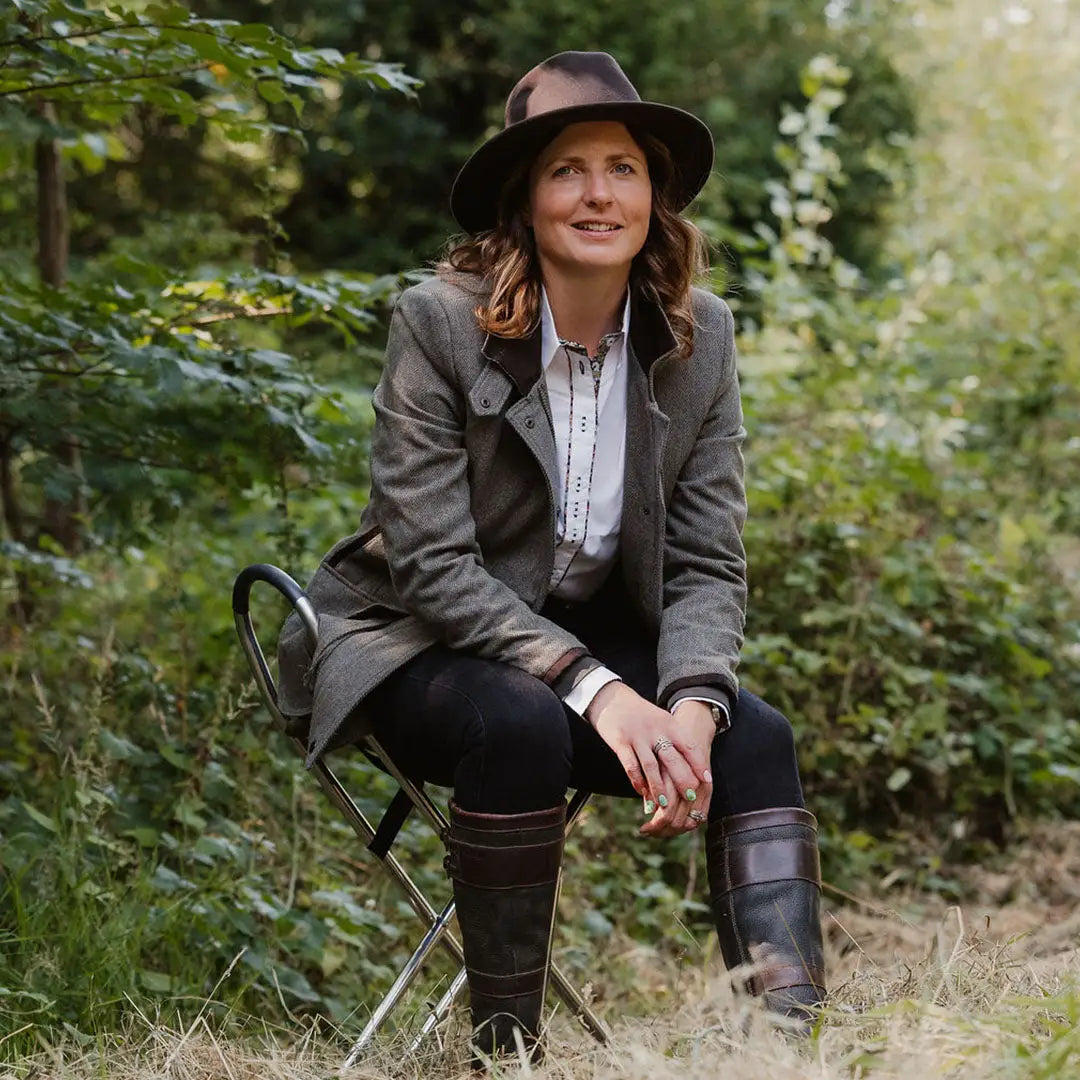 Woman in a tweed field coat sitting outdoors on a folding chair, enjoying nature