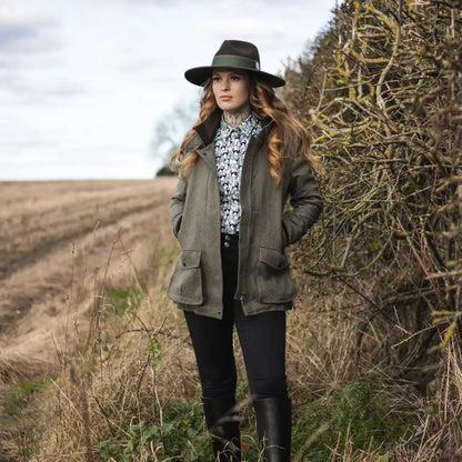 Woman in green jacket and boots by a hedgerow wearing a New Forest Tweed Field Coat